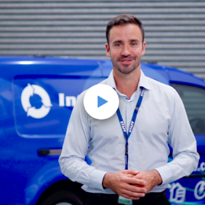 A man in front of a van. A play video symbol is visible.