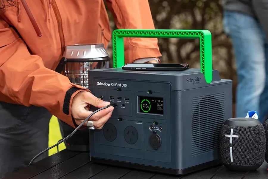 Person plugging a cable into a Schneider Off-Grid 500 portable power station on an outdoor table.