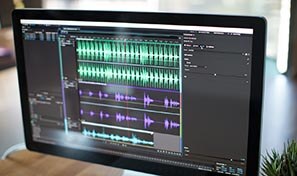 Computer monitor displaying an audio editing interface with multiple sound wave tracks arranged on a timeline.