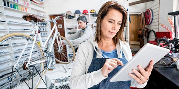 Person using tablet in bike workshop with bicycle repair in background.