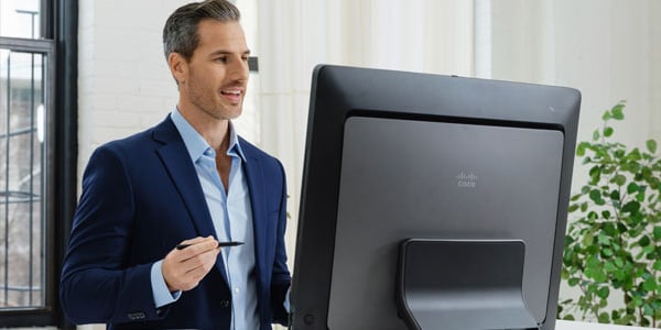 Person presenting at desk using a large Cisco monitor.