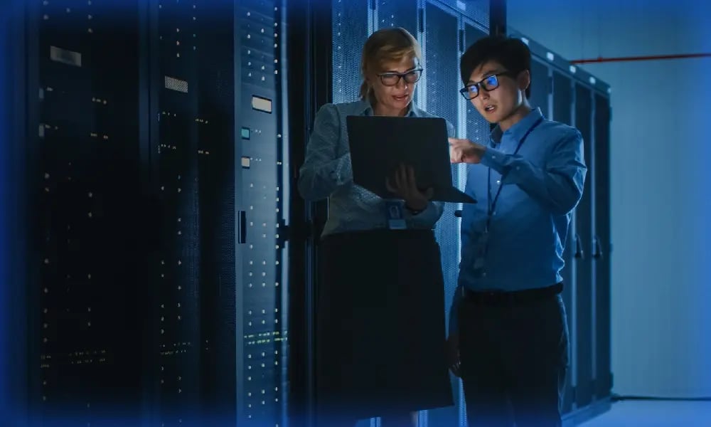 Two IT professionals reviewing a laptop together inside a data centre.