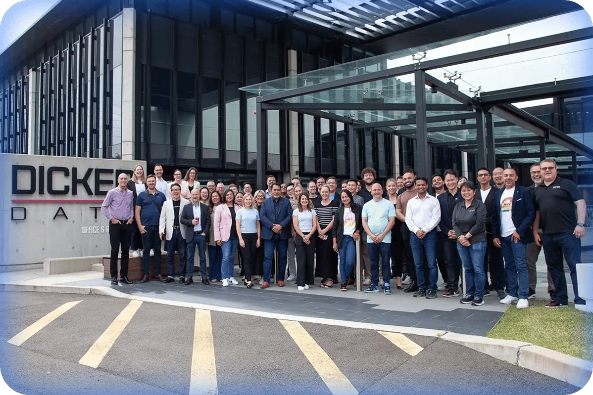A large group stands outside a corporate building with “Dicker Data” signage.