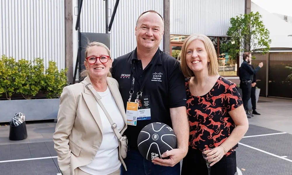 Three people stand together outdoors, one holding a basketball.