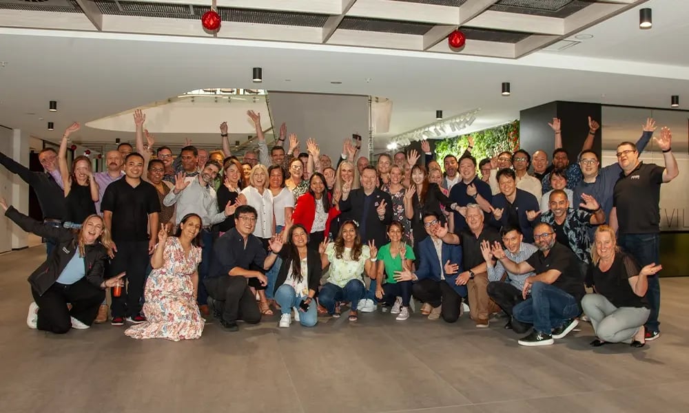 A large group of people posing together indoors with arms raised, celebrating a team or partner gathering.