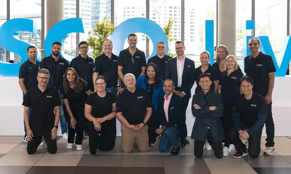 A large team poses in front of a big “Cisco Live” display inside a modern building.
