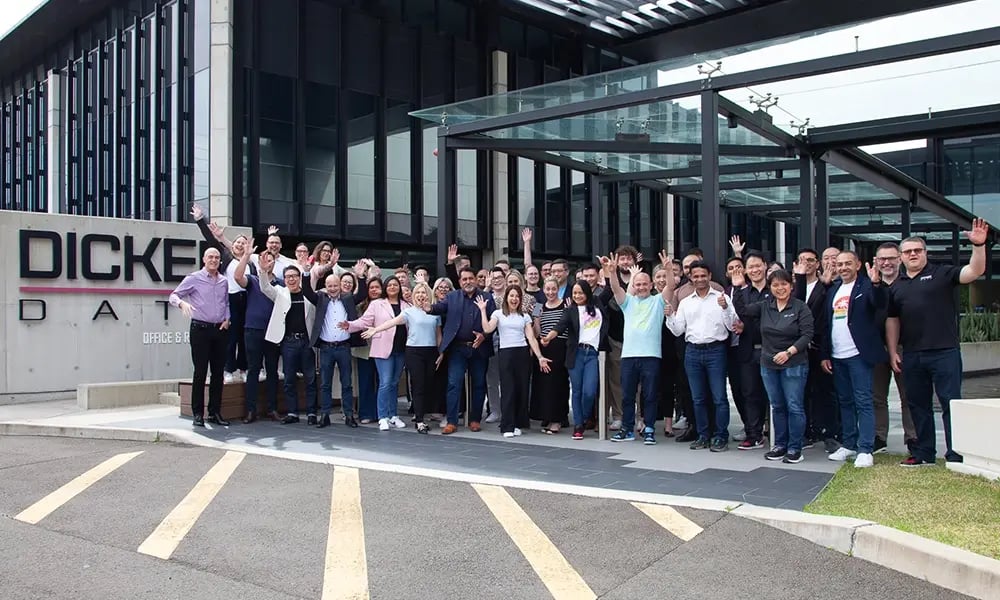A large group stands outside a corporate building with “Dicker Data” signage.