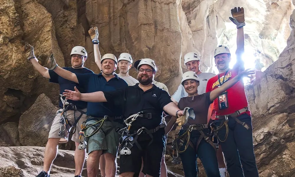 Group of people wearing helmets and harnesses inside a rocky cave.