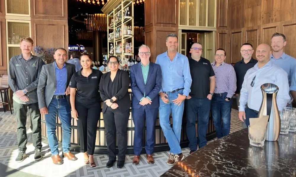 A group of people dressed in business or smart‑casual attire pose together inside a stylish bar or lounge.