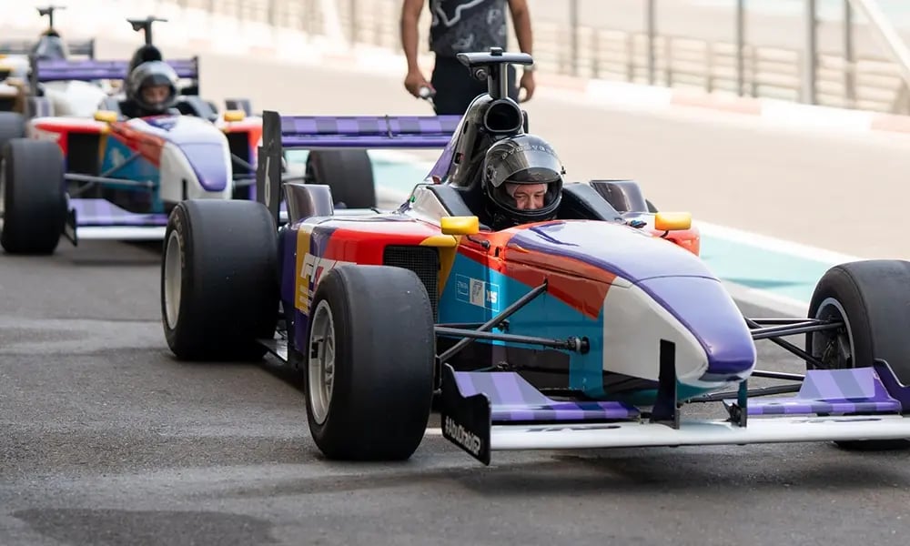 Colorful race cars lined up on a track with participants seated in the vehicles, preparing for a racing experience.