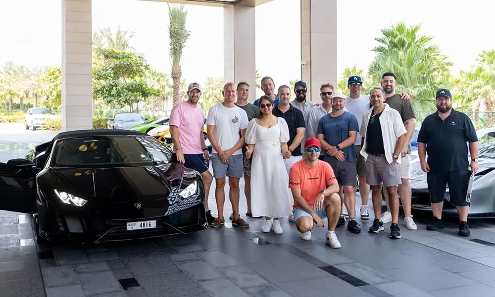 Group standing in front of two luxury sports cars near a resort entrance.