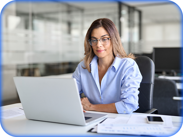 A person working on a laptop at an office desk with documents and a phone nearby.