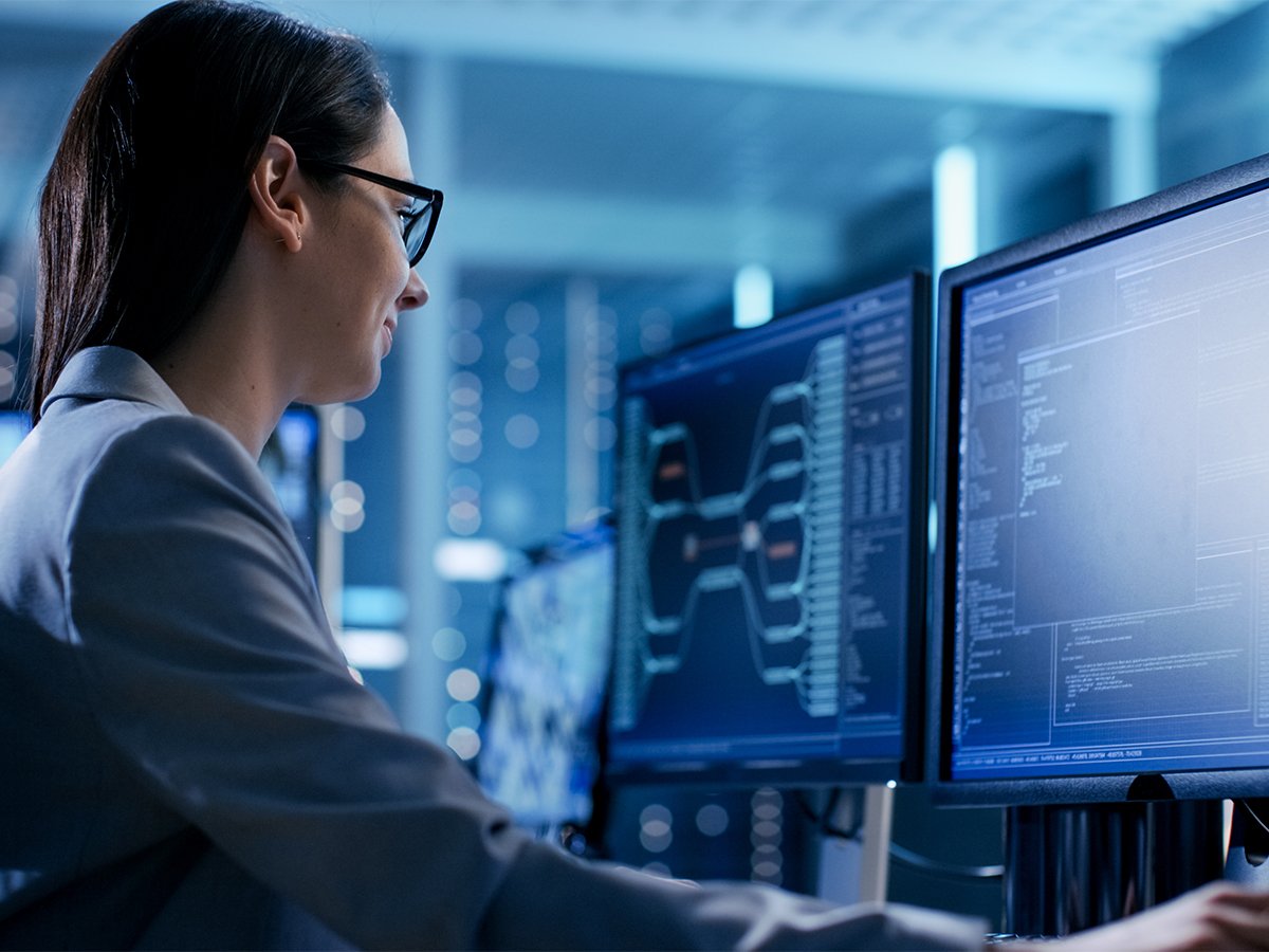 Person working at a desk with multiple computer monitors displaying complex data and code in a modern technology environment.