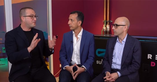 Three people seated and talking in a studio interview setting.