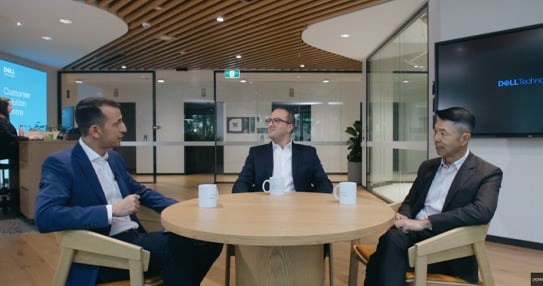 Three people seated around a table, talking in a meeting room.