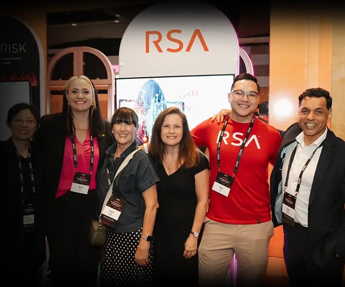 Group of conference attendees posing at an RSA booth, standing in front of a branded display screen
