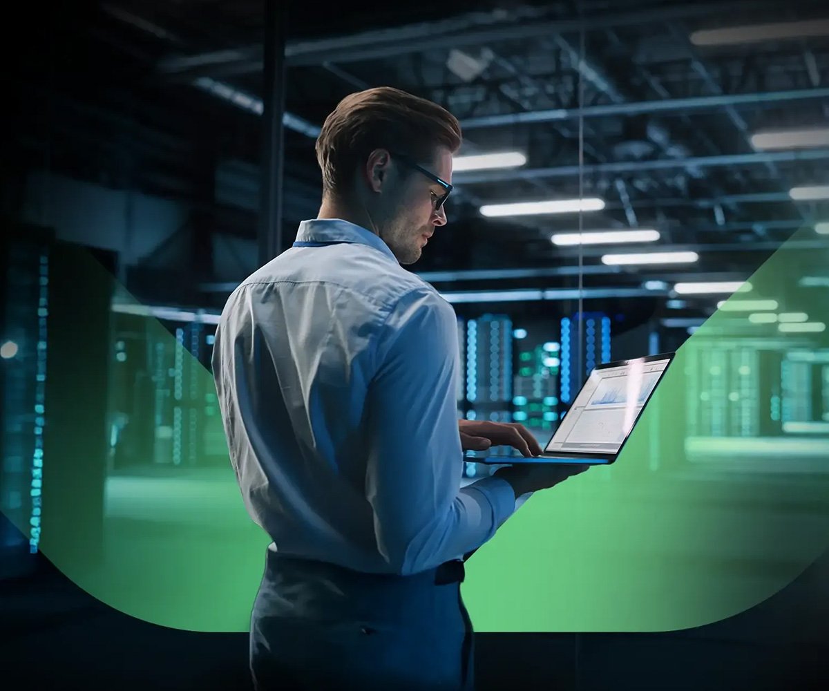 Person using a laptop in a data centre, reviewing analytics on screen with server racks in the background