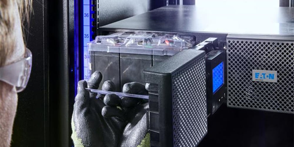 Person wearing safety gloves installing a battery module into an Eaton UPS system.