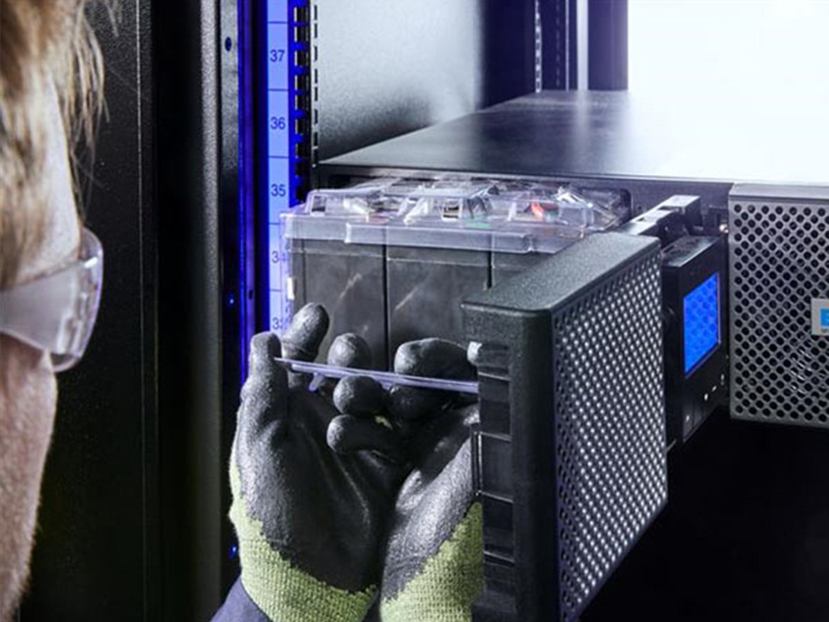 Person wearing safety gloves installing a battery module into an Eaton UPS system.