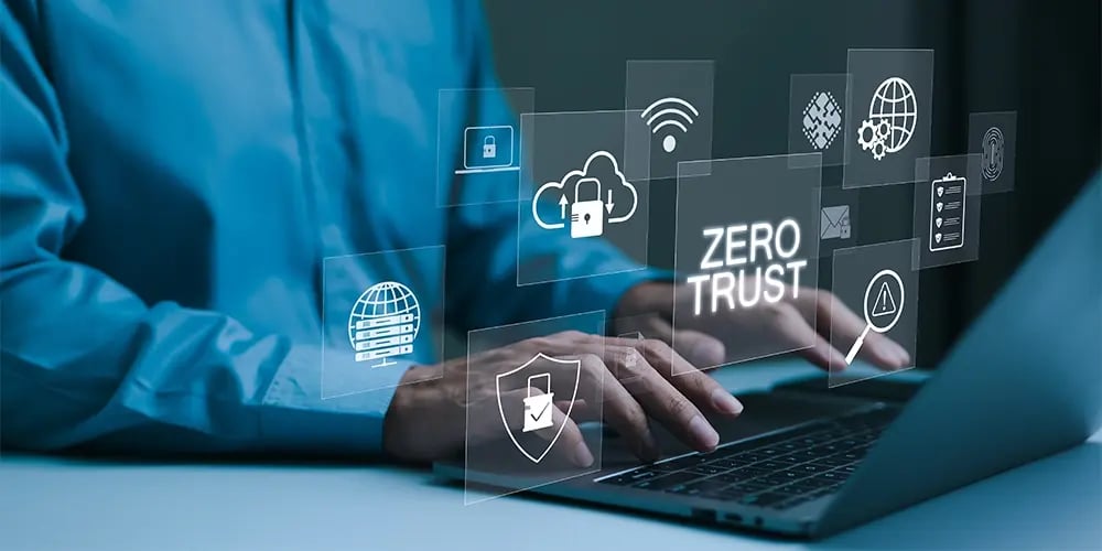 Hands typing on a laptop with floating digital security icons and the words ‘Zero Trust.’
