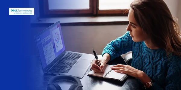 Person writing in a notebook while using a Dell laptop on a desk.