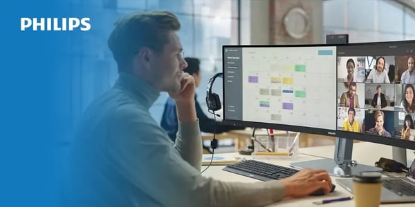 Person working at a desk with a Philips ultra-wide monitor showing a calendar and video call interface.