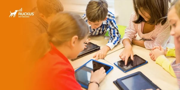 Group of children using tablets on a table in a classroom setting.