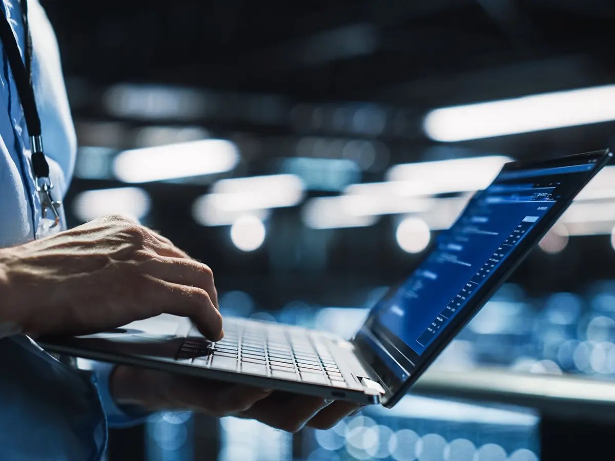 Hands typing on a laptop in a server room.
