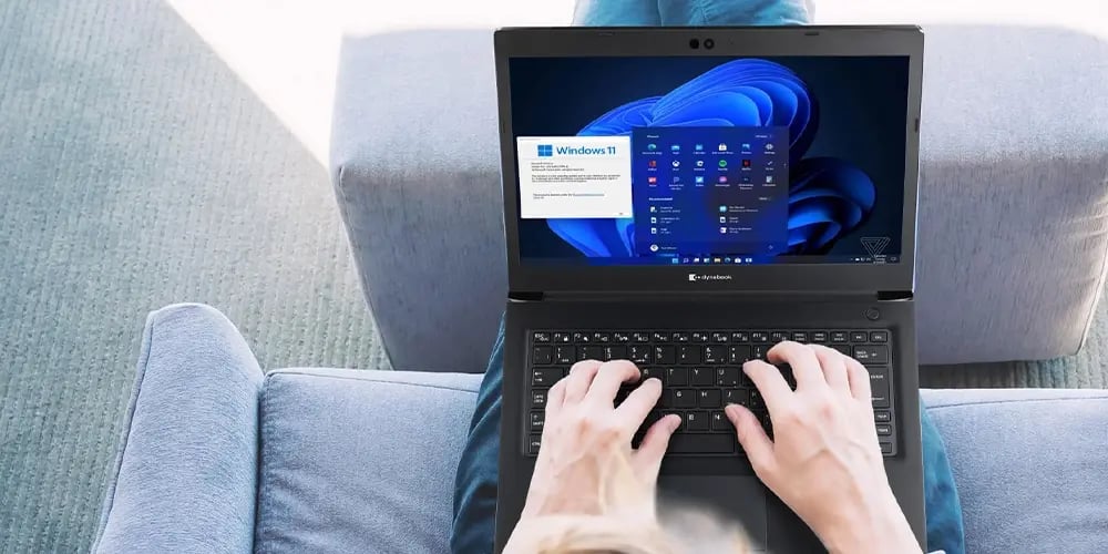 Laptop displaying the Windows 11 home screen and setup window, placed on a person's lap while typing.