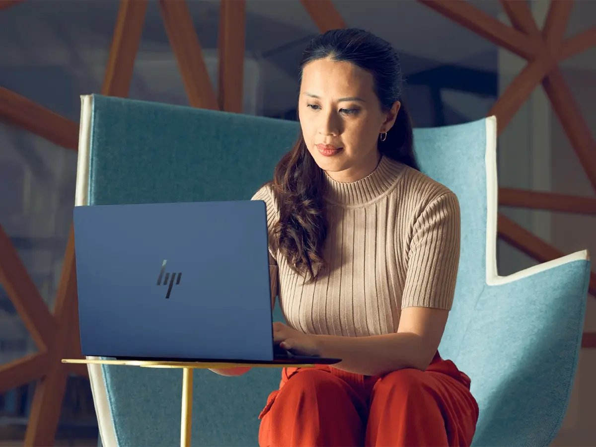 Person using an HP laptop while seated on a modern chair, representing an AI-powered notebook for productivity.