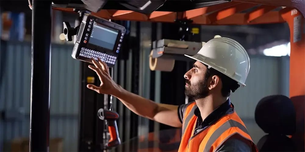 Worker wearing a safety vest and hard hat operating a mounted scanner on industrial equipment.