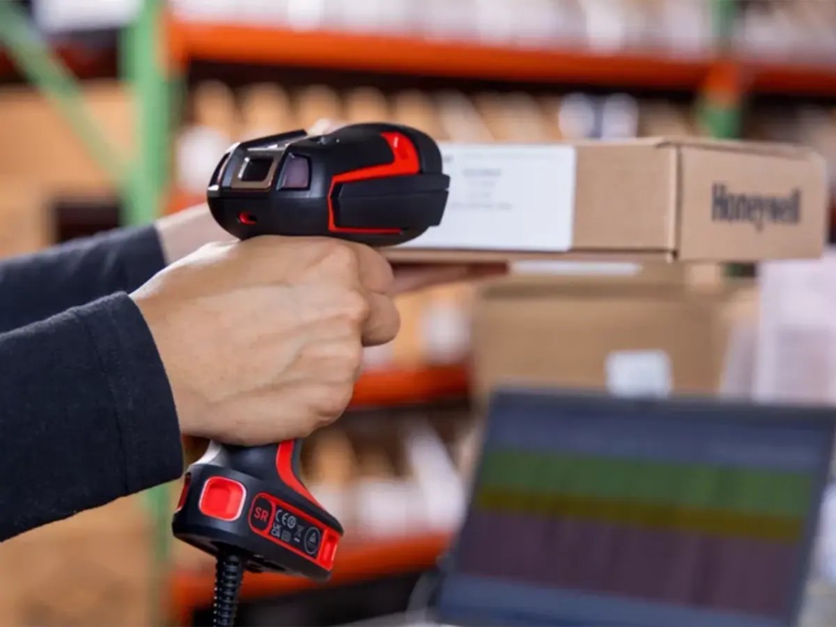 Person using a handheld barcode scanner to scan a box in a warehouse setting.