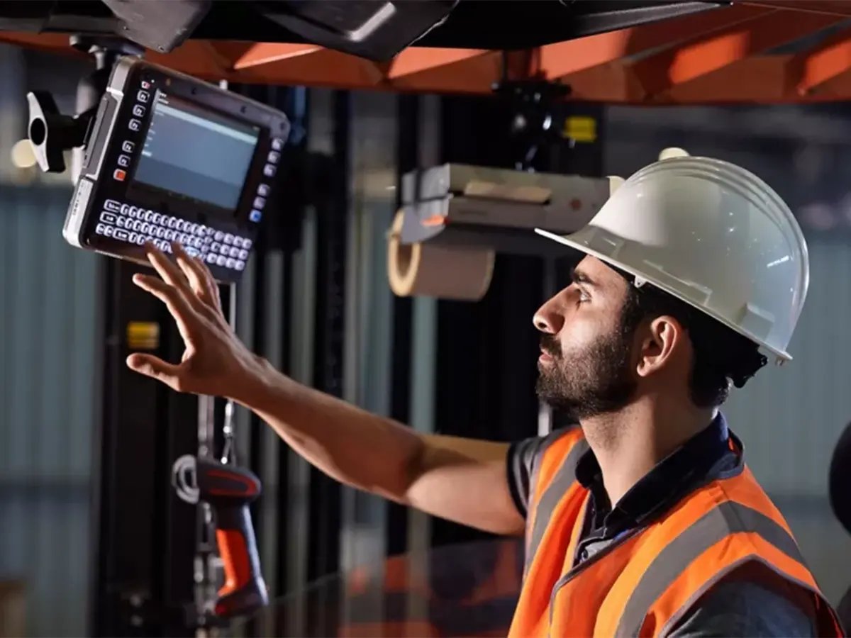 Worker wearing a safety vest and hard hat operating a mounted scanner on industrial equipment.