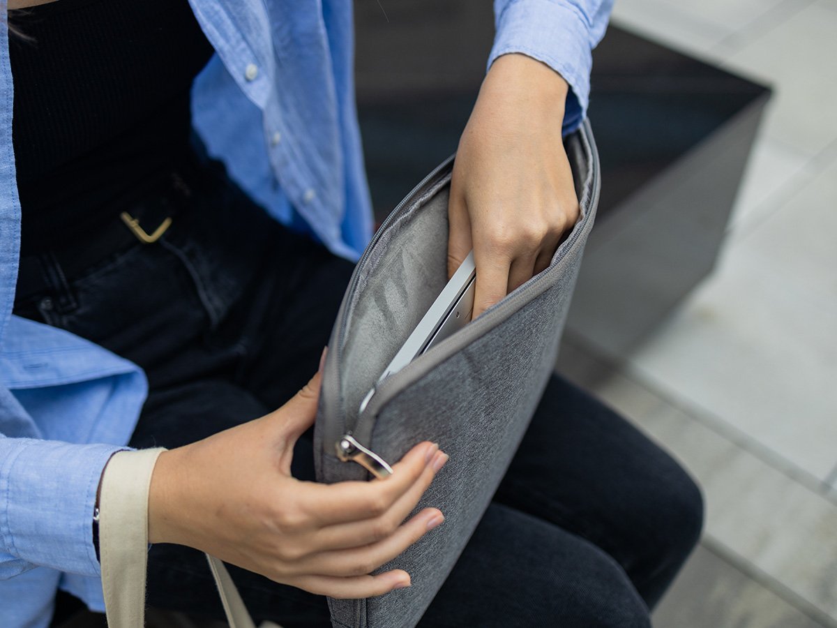 Person sliding a laptop into a grey fabric sleeve while seated.