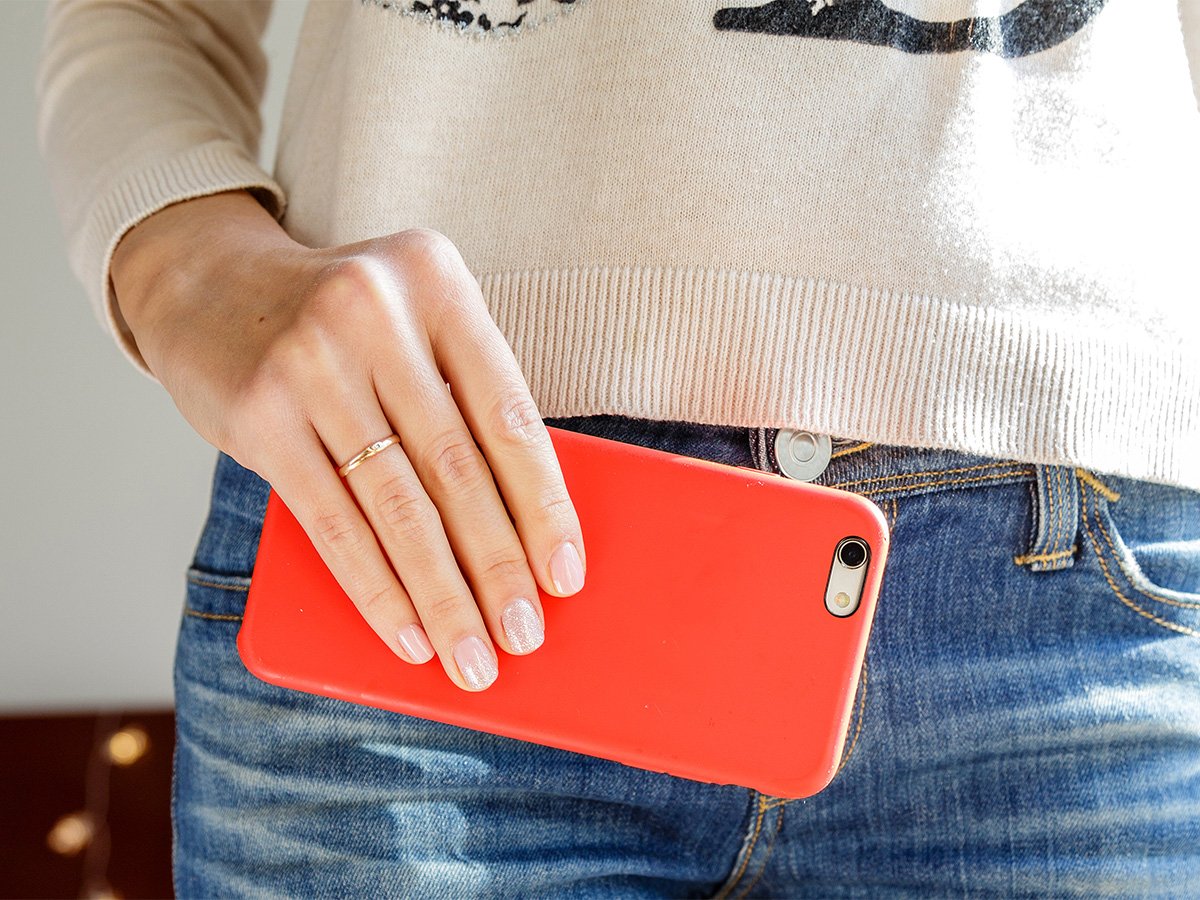 Hand holding a smartphone against a person’s jeans pocket.