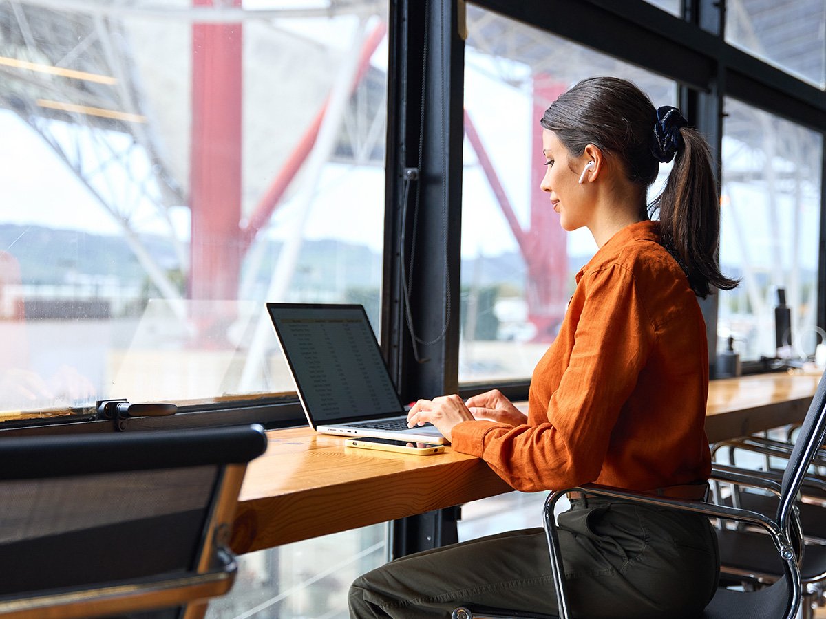 Person working on a laptop at a desk beside a large window in a modern office setting.