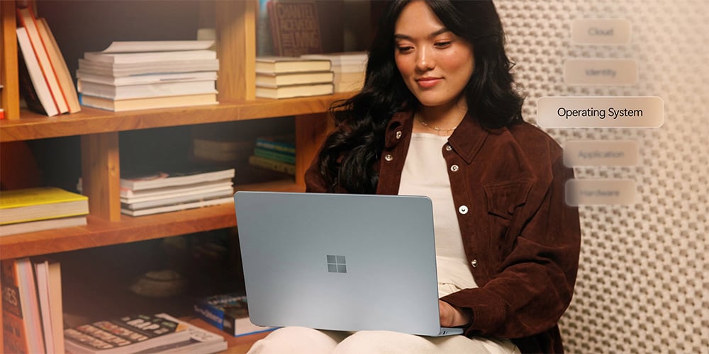 Person using a silver laptop while seated near a bookshelf.