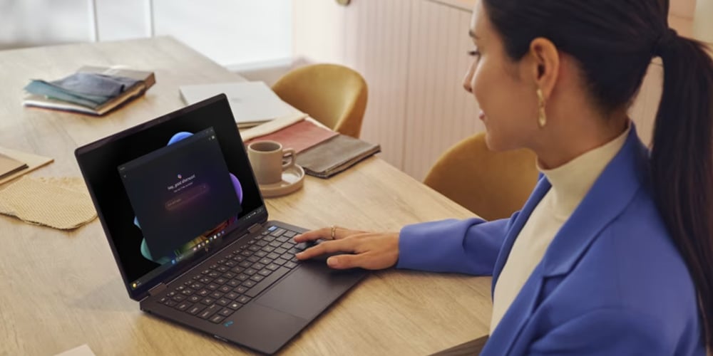 Person working on a laptop at a wooden table with notebooks and a coffee cup.