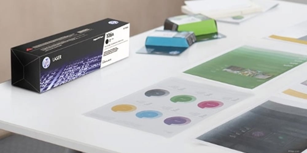 HP Laser toner cartridge box on a desk with color charts and papers.