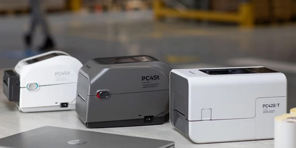Three Honeywell desktop label printers placed on a table with a laptop.