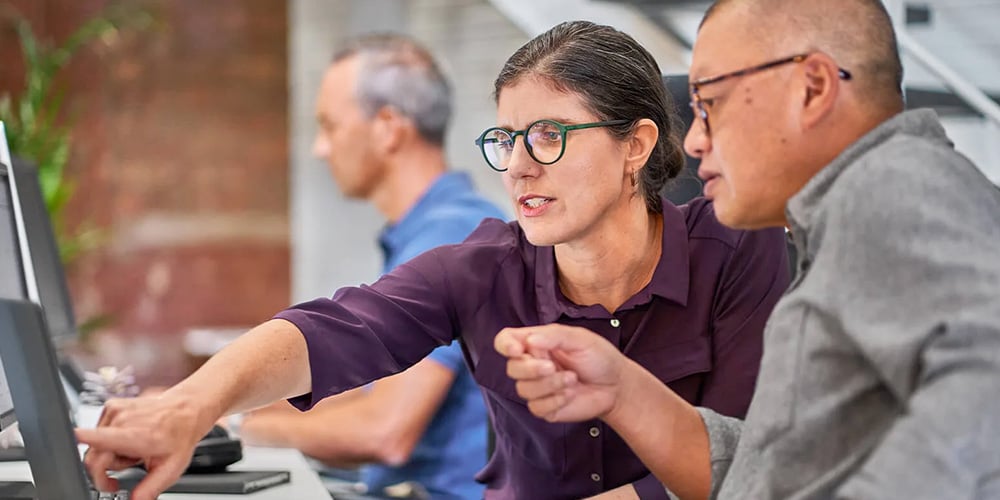 Person pointing at a computer screen during a discussion in an office setting.