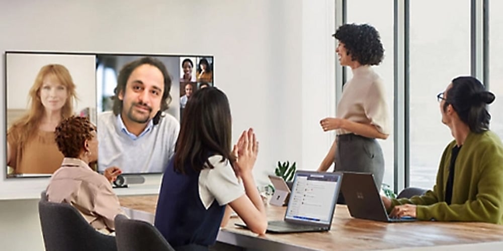 Office team gathered around a table while viewing remote participants on a large video screen.