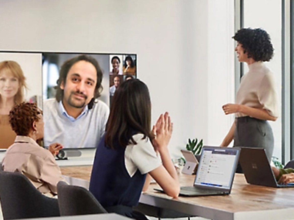 Office team gathered around a table while viewing remote participants on a large video screen.