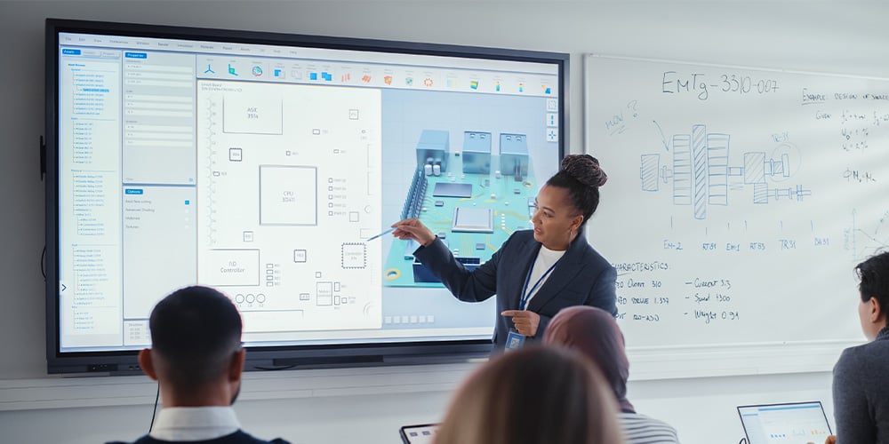Presenter explaining a technical diagram on a large interactive display to a seated audience.