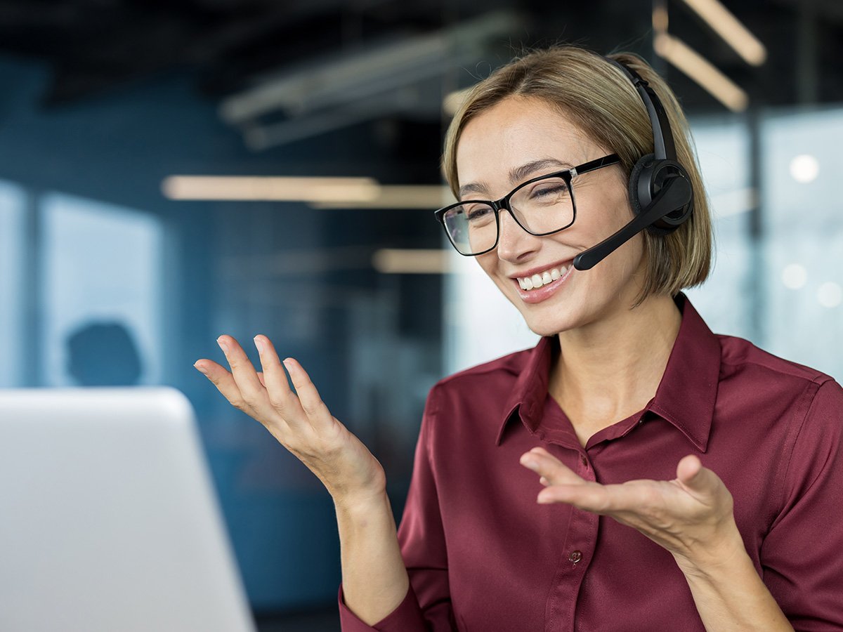 Person wearing a headset speaking and gesturing during a video call at a desk.