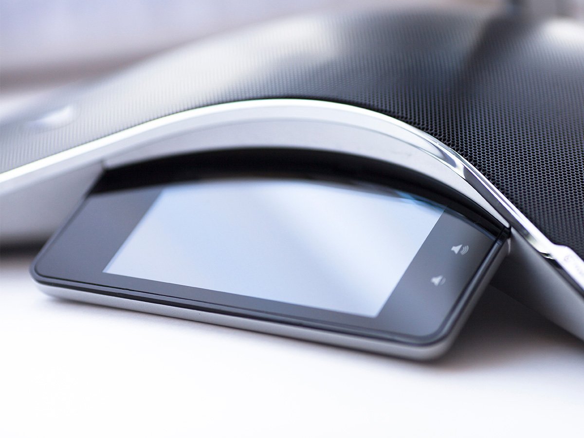 Close-up of a modern conference speakerphone with a touchscreen control panel.
