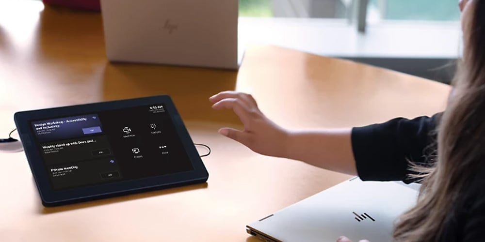 Person using a touchscreen meeting control panel on a table.