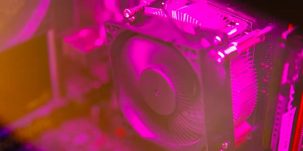 Close‑up of a computer cooling fan inside a PC case, lit with pink and purple lighting.
