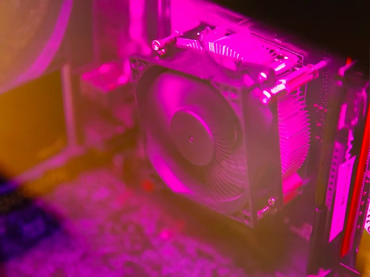 Close‑up of a computer cooling fan inside a PC case, lit with pink and purple lighting.