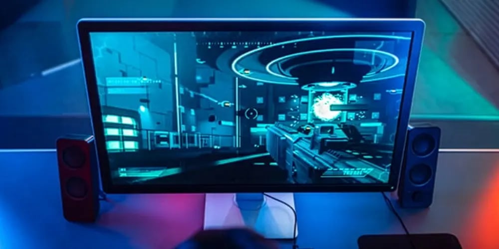 Overhead view of a desktop monitor showing a first‑person video game, with keyboard, mouse, speakers, and blue lighting.